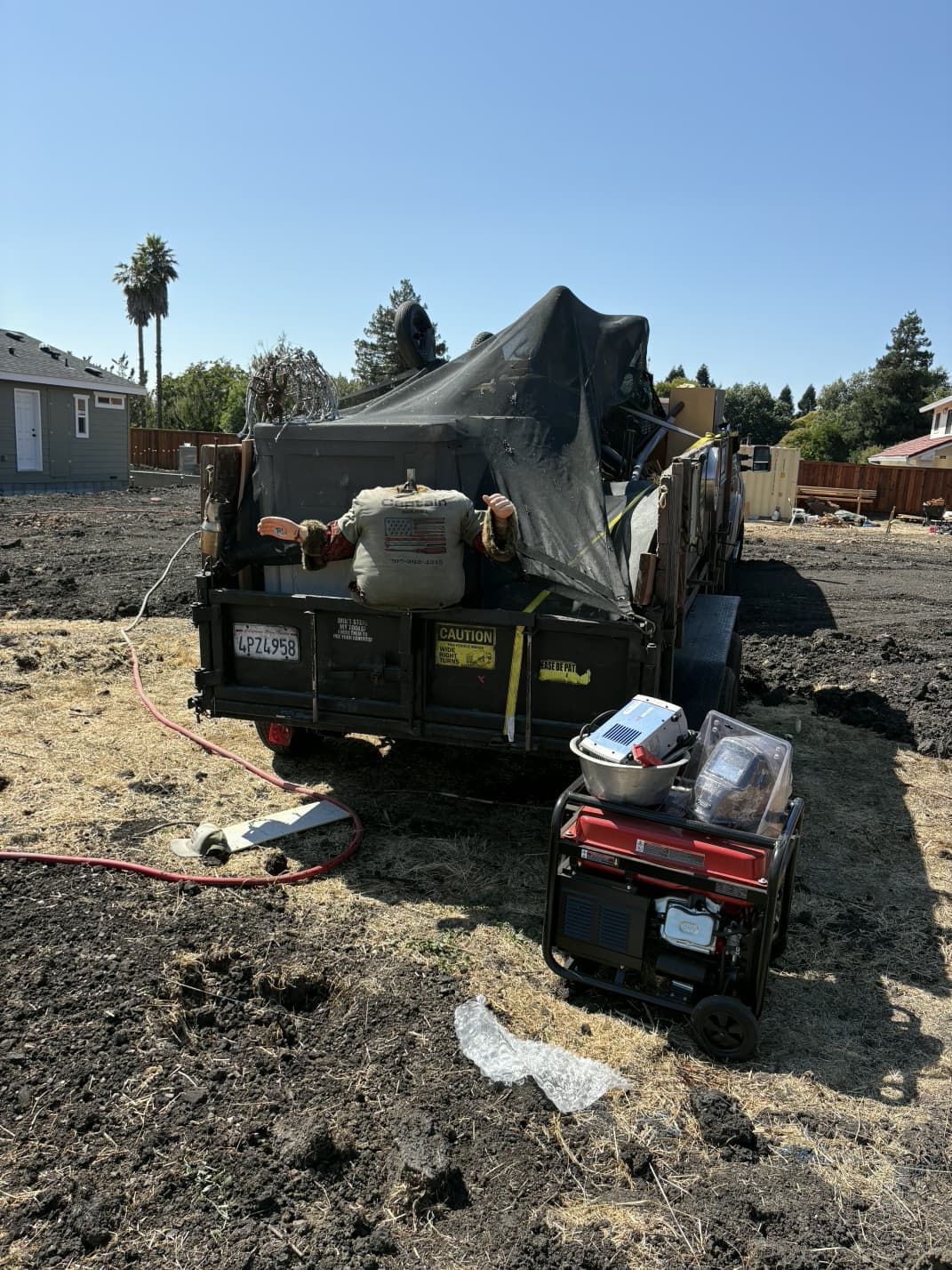 Rear view of hauling trailer secured with tarp and tools at job site.