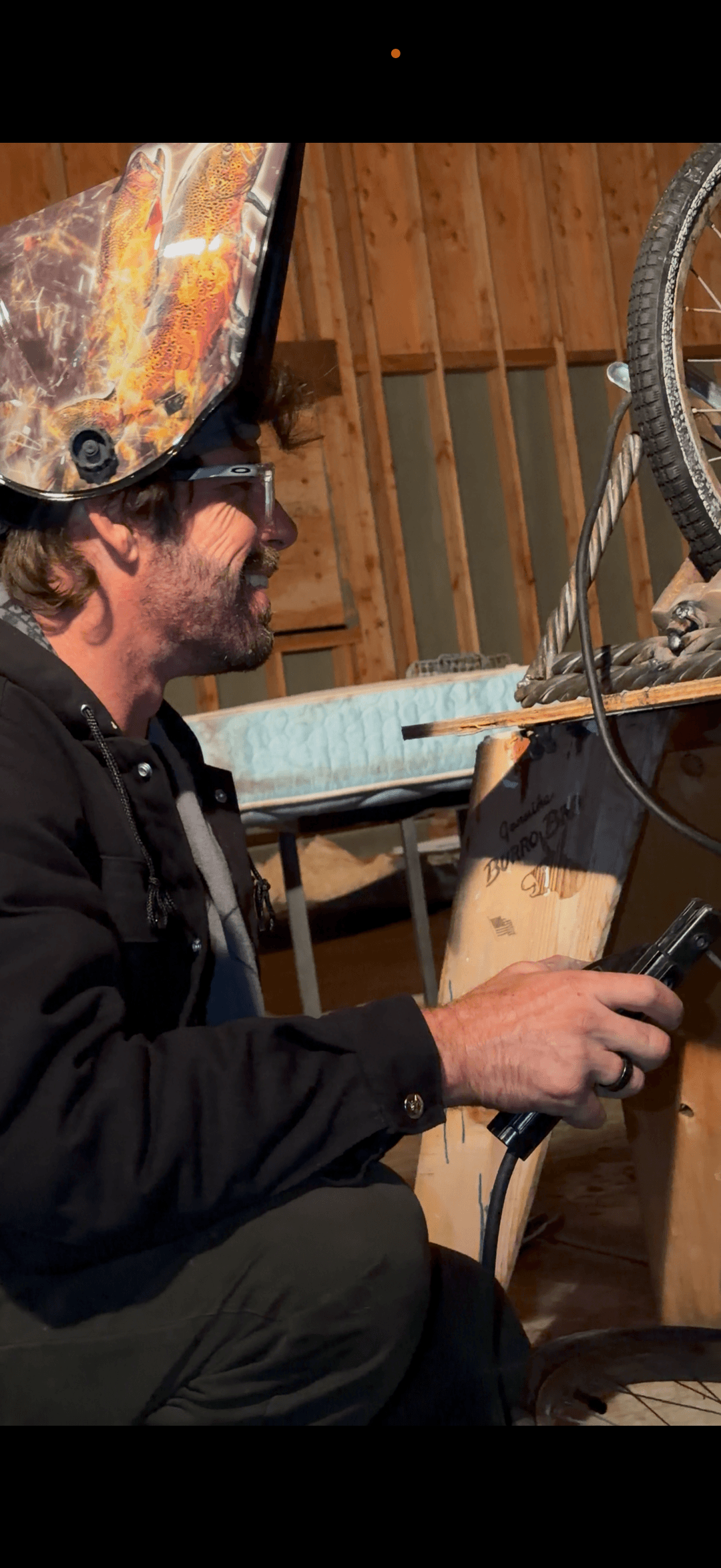 Worker welding indoors wearing protective helmet and safety glasses during fabrication work.