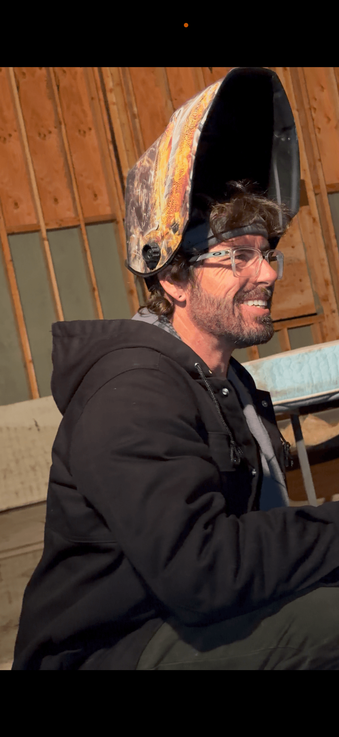 Close-up of worker smiling in welding helmet and safety glasses inside workshop.